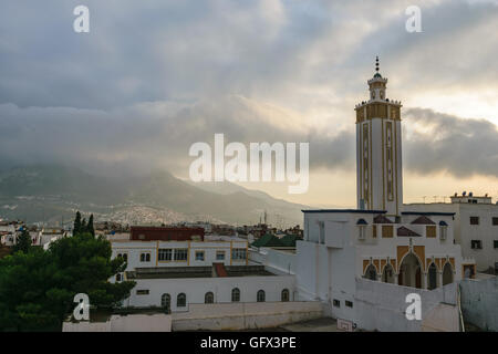 Schöner Ausblick über Tetouan und eine Moschee mit den Bergen bedeckt in Wolken im Hintergrund und einem schönen Sonnenuntergang mit goldenen li Stockfoto