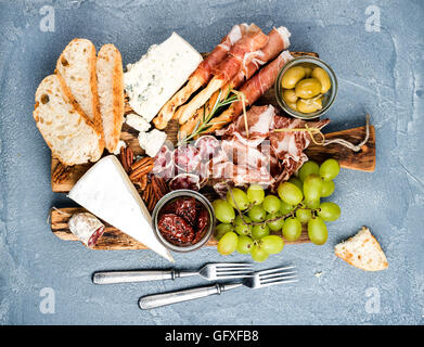 Käse und Fleisch Vorspeise Auswahl oder Wein Snack festgelegt. Vielzahl von Salami, Schinken, Brot-Sticks, Baguette, Honig, Trauben, Oliven, getrocknete Tomaten, Pecan-Nüssen über grauem Beton texturiert Kulisse, Draufsicht. Stockfoto