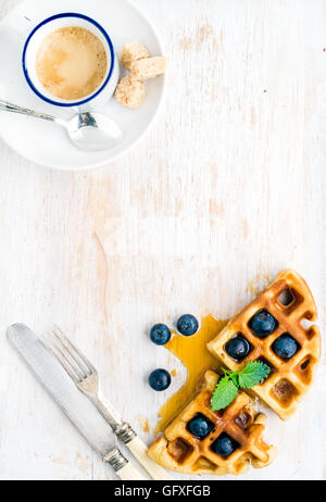 Espresso-Kaffee-Tasse, weiche belgische Waffeln mit frischen Heidelbeeren und Marple Sirup auf weiß lackiertem Holzbrett auf hellblauem Hintergrund Stockfoto