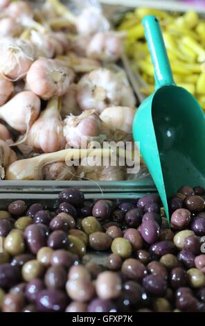 Oliven und Knoblauch. Würzige schwarze Oliven, eingelegte Knoblauch Kopf und grüne Chili mit Soße in einem Markt stehen. Nahaufnahme von Vorspeisen und Essiggurken Stockfoto