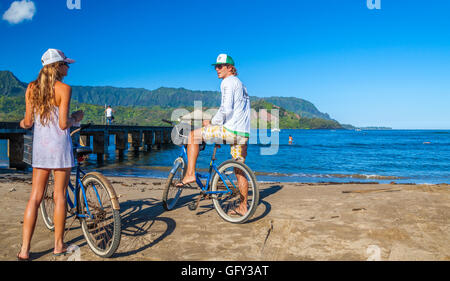 Touristen mit Fahrrädern durch den Hanalei Pier auf Kauai mit SUP und Mt. Makana genannt Bali Hai in Ferne Stockfoto