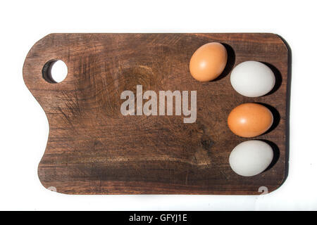 vier Eiern, zwei rote und zwei weiße, auf einem Holzbrett isoliert auf weißem Hintergrund Stockfoto