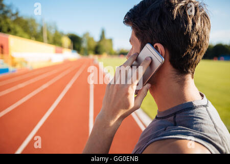Seitenansicht eines männlichen Athleten auf der Laufstrecke stehen und telefonieren mit Handy Stockfoto