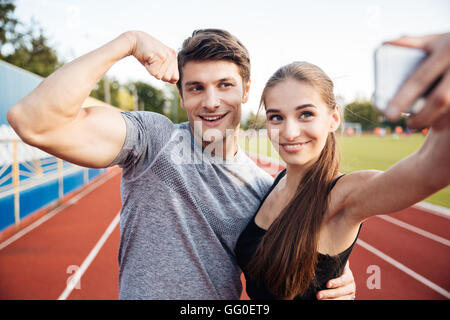 Happy Young Sport paar machen Selfie Foto auf Stadion, Mann zeigt Bizeps vor der Kamera Stockfoto