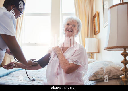 Messung des Blutdrucks senior Frau Ärztin. Ältere Frau auf Bett lächelnd während Krankenschwester überprüfen ihr Blut Stockfoto