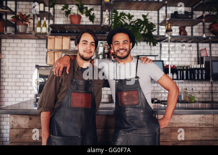 Porträt von zwei jungen Coffee-Shop-Besitzer stehen zusammen an der Bar-Theke und Blick in die Kamera. Stockfoto