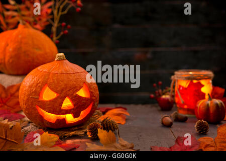 Brennen von Jack O'Lantern auf einem rustikalen Tisch mit herbstlichen Dekorationen, beleuchtet dunkel. Stockfoto