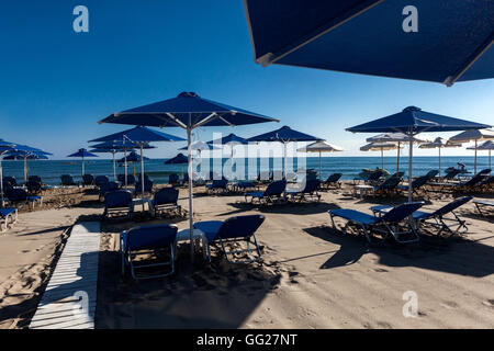 Sonnenschirme und Sonnenliegen am blauen Eingang zum Strand von Rethymno, Kreta Strand Griechenland, Strand bereit für die Ankunft von Urlaubern Stockfoto