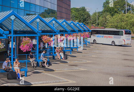 National Express Bus in Bournemouth Coach Station, Bournemouth, Dorset UK mit Menschen warten und bunte hängenden Körbe im Juli - hdr-Effekt Stockfoto