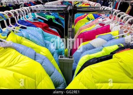 Vielzahl von Winterkleidung auf Metall Kleiderbügel. Bunten Winterjacken hängen Kleiderbügel auf einem Gestell in einem Geschäft Stockfoto