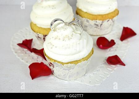 Trauringe in Cupcake Icing mit Sterne Streuseln und rote Rosenblüten auf Papier Herz Deckchen. Stockfoto