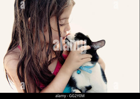 Ein junges Mädchen küsst sanft ihre schwarz-weiße Katze und zeigt einen süßen und liebevollen Moment der Liebe zwischen einem Kind und ihrem Haustier Stockfoto