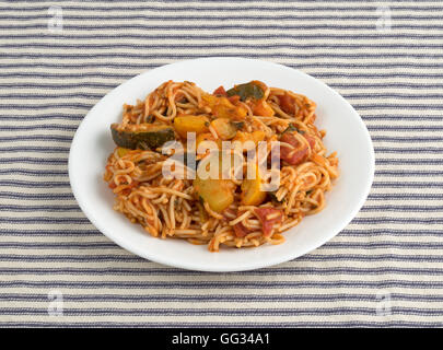 Angel Hair Pasta mit Zucchini und Spinat auf einem weißen Teller oben auf eine gestreifte Tischdecke. Stockfoto