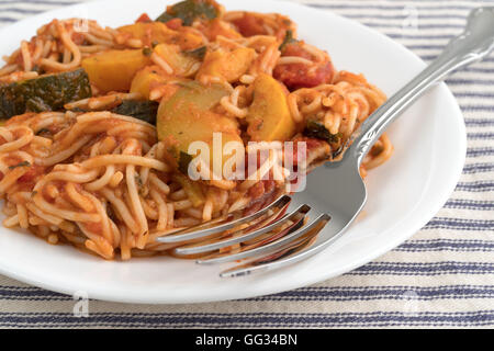 Angel Hair Pasta mit Zucchini und Spinat auf einem weißen Teller mit einer Gabel oben auf eine gestreifte Tischdecke. Stockfoto