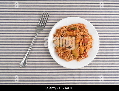Draufsicht der Engel Haar Pasta mit Zucchini und Spinat auf einem weißen Teller mit einer Gabel auf der Seite oben auf eine gestreifte Tischdecke. Stockfoto