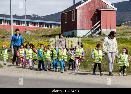 Lokale Schulkinder tragen hi-Vis Jacken und Hand in Hand entlang einer Straße mit ihren Lehrern im Sommer 2016. Narsaq Grönland Stockfoto