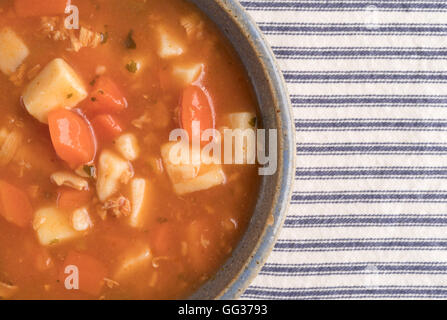 Enge Draufsicht einer Portion Manhattan Stil Muschelsuppe in einer alten Steingut-Schüssel auf gestreifte Tischdecke. Stockfoto