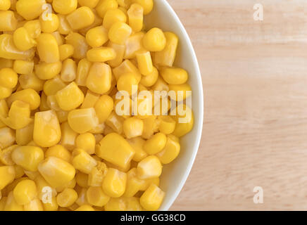 Enge Draufsicht einer Portion Bio aus der Dose Zuckermais in einer kleinen weißen Schüssel auf einem Holztisch. Stockfoto