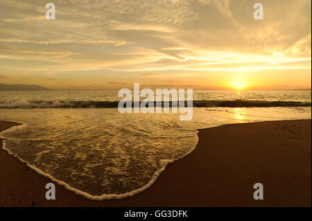 Meer Sonnenuntergang ist ein hell am Strand mit den Sonnenuntergang am Meer Horizont wie eine sanfte Welle entlang der sandigen Küste rollt. Stockfoto