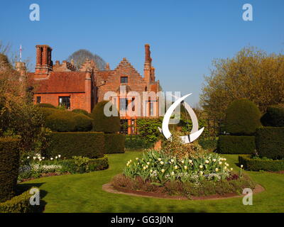 Chenies Manor weiße Garten mit Blick auf das Haus. Rundes Beet mit Tulpen, Skulptur, Hecke, Rasen und blauer Himmel Stockfoto