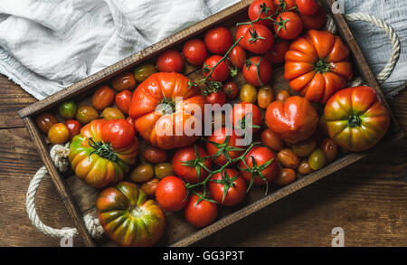 Bunte Tomaten in verschiedenen Größen und Arten in dunklen Holztablett über rustikale Hintergrund Stockfoto