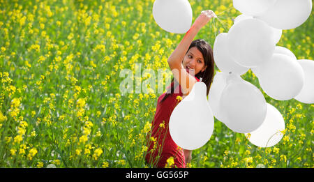 Junge Frau mit Luftballons in einem Feld Stockfoto