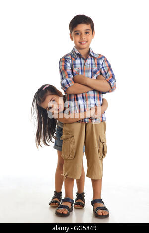 Porträt von lächelndes Mädchen umarmen Bruder von hinten vor weißem Hintergrund Stockfoto