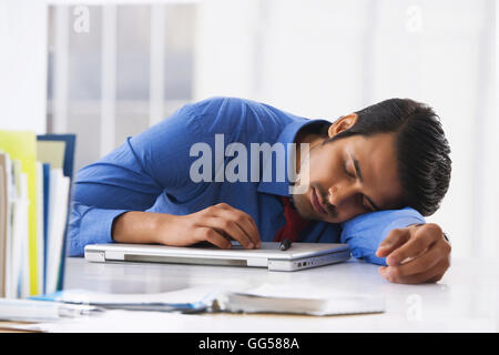 Junge indische Geschäftsmann auf Laptop am Schreibtisch schlafen Stockfoto