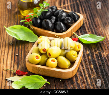 Bio grüne und schwarze Oliven in Holzschalen mit Basilikum, Oregano und Gewürzen. Mediterrane Küche Stockfoto