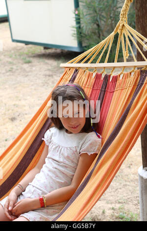 wunderschönes kleines Mädchen mit langen braunen Haaren ruht auf einer Hängematte im Sommer Stockfoto