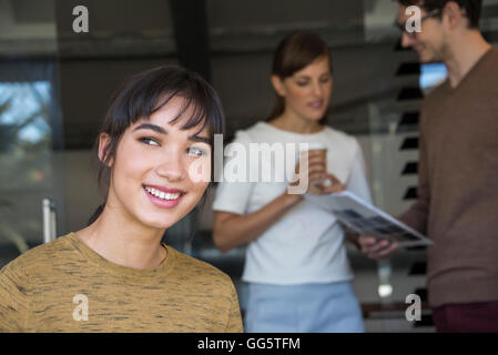 Eine schöne Geschäftsfrau mit ihren Kollegen im Hintergrund lächelt in Nahaufnahme Stockfoto