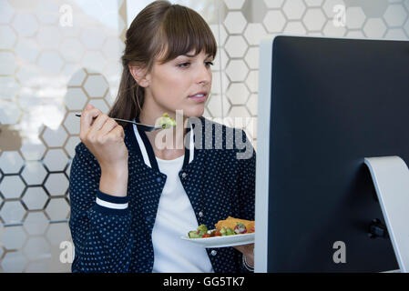 Schöne Frau vor dem Computer sitzen und Essen Stockfoto