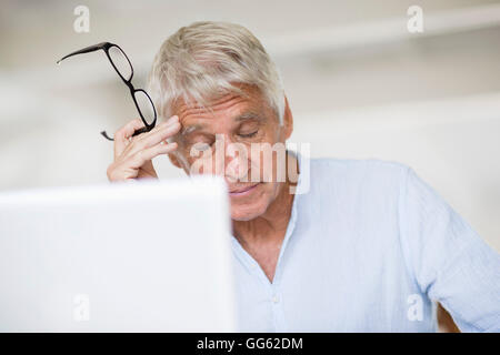 Müde senior woman Kopf in der hand mit Laptop auf Tisch Stockfoto