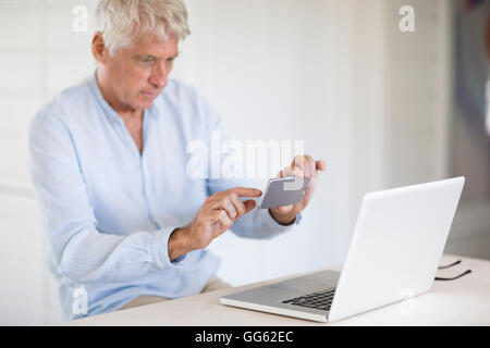 Senior woman fotografieren Laptop-Bildschirm mit Kamera-Handy Stockfoto