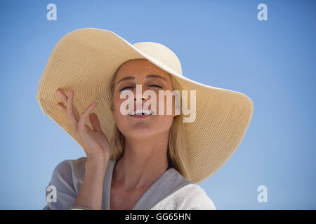 Porträt der glückliche junge Frau Sonnenhut am Strand zu tragen Stockfoto