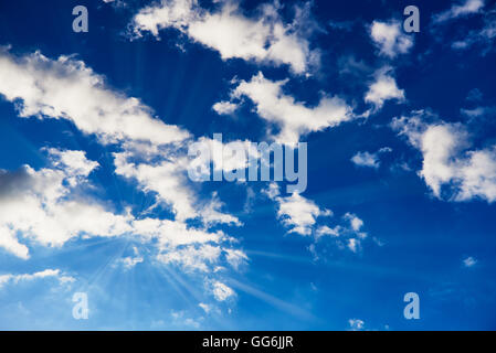 Blauer Himmel mit weißen Wolken, die Sonne mit sichtbaren Sonnenstrahlen Stockfoto