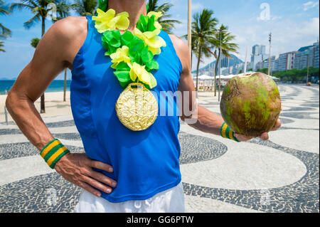 Goldmedaille Athlet stehend mit grünen Kokosnuss Coco Gelado hängend Lei auf der Promenade am Strand der Copacabana, Rio De Janeiro Stockfoto
