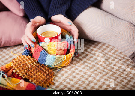 Weiche gemütliche Foto von schlanke Tan Frau in warmen Pullover auf dem Bett mit Tee in Händen, Ansicht von oben Punkt. Mädchen sitzen auf kariertes Karo in der Nähe und Cookies. Stockfoto