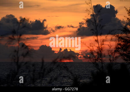 Brilliant orange Sonnenuntergang mit schwarzen Wolken an einem tropischen Strand Stockfoto