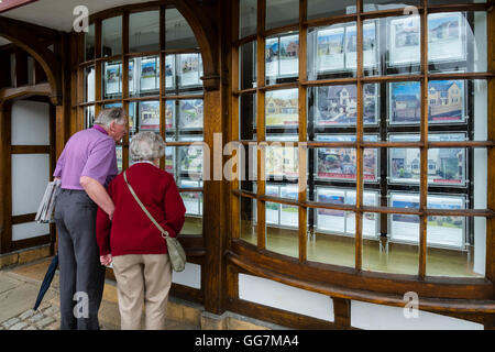 Älteres Paar sucht in Immobilienmakler Fenster an Immobilien zum Verkauf in den Cotswolds im England, United Kingdom Stockfoto