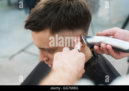 Professionelles Styling. Seitenansicht des jungen Mannes immer Haarschnitt von Friseur mit Elektrorasierer bei Barbershop hautnah Stockfoto