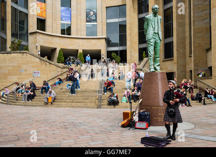 Menschen, die draußen in der Sonne sitzen auf Schritte der Glasgow Royal Concert Hall mit Busker Dudelsack in Glasgow, Schottland, Einheit Stockfoto