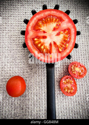 Eine halbe Tomate auf einer verzahnten Kochlöffel auf grauem Grund. Vertikales Bild. Stockfoto