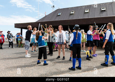 Frauen, die beide von Morris Seiten und Mitglieder der Öffentlichkeit, tanzen die 'gun Dance" mit hölzernen Stäben als Waffen, während auf Broadstairs Harbour Jetty. Stockfoto