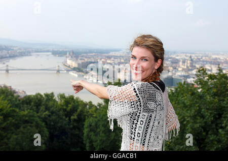 Glückliche junge rothaarige Frau zeigt Weg Budapest Panorama, Lächeln Zähne Stockfoto