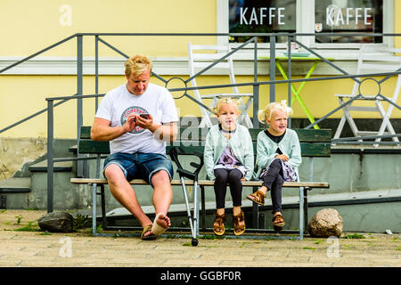 Ystad, Schweden - 1. August 2016: Echte Menschen im Alltag. Erwachsener Mann mit Krücken und einem verletzten Fuß sitzen neben zwei schöne Mädchen Stockfoto