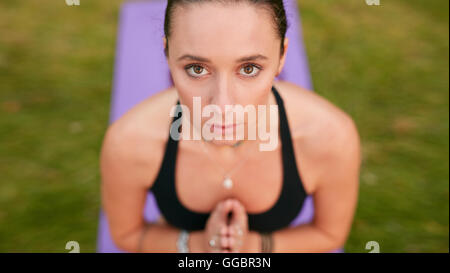 Schuss der selbstbewusste junge Frau mit gefalteten Händen zu meditieren und Blick in die Kamera hautnah. Kaukasische Fitness weibliches Modell pract Stockfoto