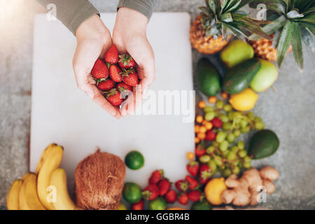 Draufsicht-Aufnahme einer Frau übergibt halten frische Erdbeeren Schneidebrett mit Früchten. Frau mit einer Handvoll frische str Stockfoto