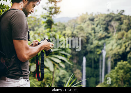 Mann stand vor Wasserfall mit Digitalkamera und überprüfen die Bilder. Männliche Wanderer fotografieren einen Wasserfall in fores Stockfoto