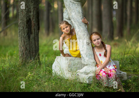 Zwei niedliche kleine Mädchen sitzen auf einem alten Sockel im Park. Stockfoto